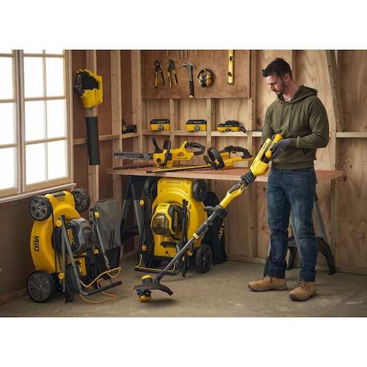 STANLEY SFMCBLB76B blower in use, surrounded by yellow STANLEY tools and lawn mowers in a workshop setting.